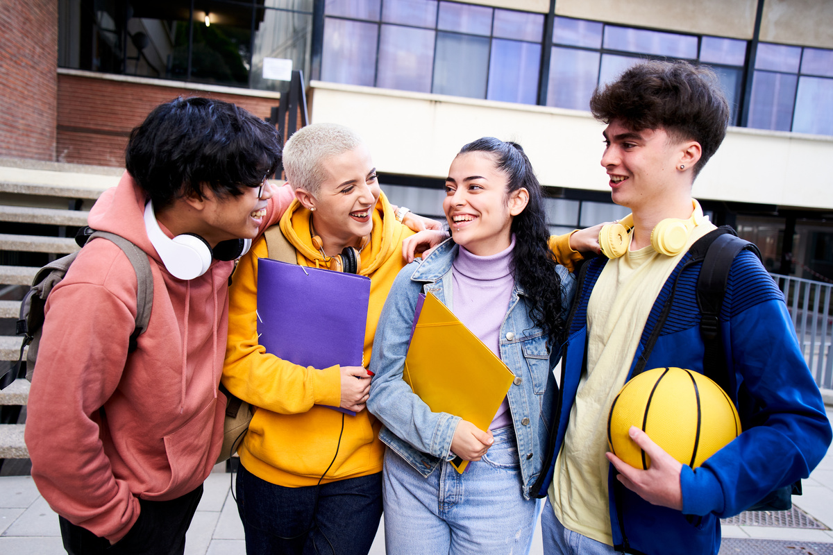 Group of gen z classmate and friends having fun outdoors high school. They hug each other cheerful